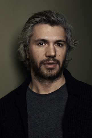 Nicolai Cleve Broch in a black sports jacket and grey round neck t-shirt on a brown background